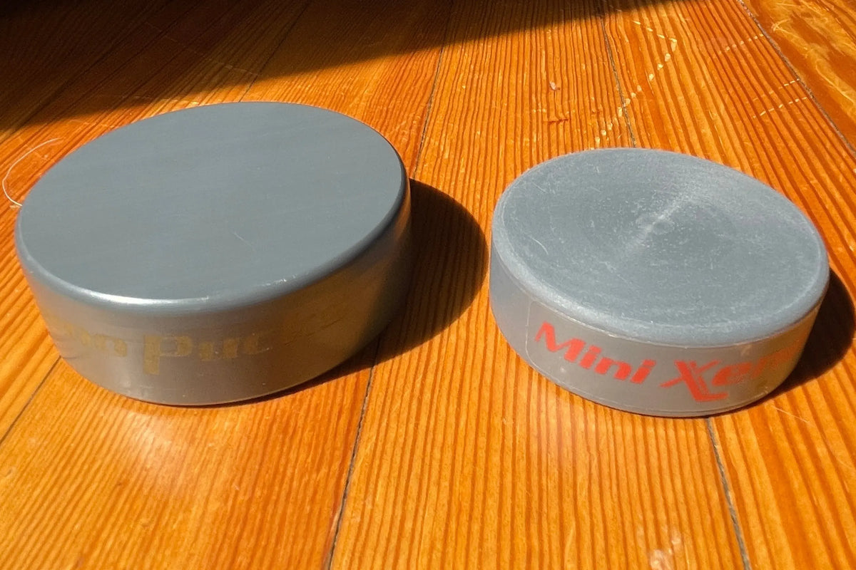 Mini Xeno next to a regular Xenopuck, resting on a wooden floor in direct sunlight.
