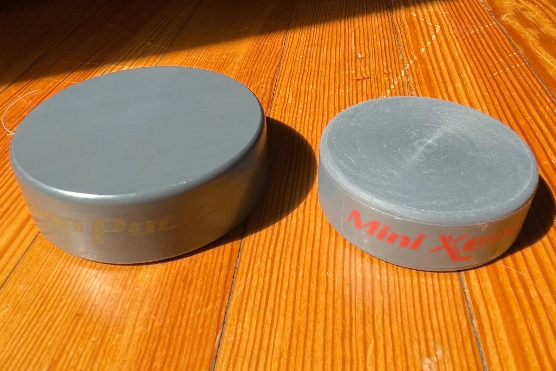 Mini Xeno next to a regular Xenopuck, resting on a wooden floor in direct sunlight.