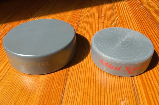 Mini Xeno next to a regular Xenopuck, resting on a wooden floor in direct sunlight.